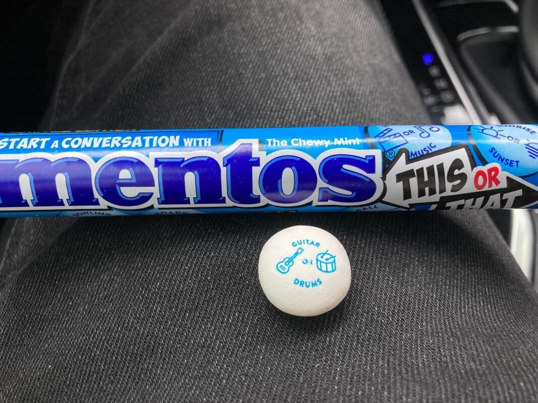 picture of a roll of Mentos chewy mints with one small, round mint with the words guitar or drums
