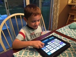 A young boy is sitting at a kitchen table interacting with an iPad.